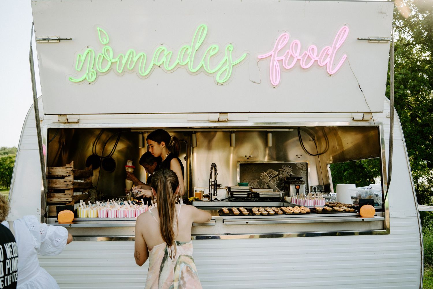 Nomades Food truck with neon sign serving guests at outdoor wedding reception at dusk.