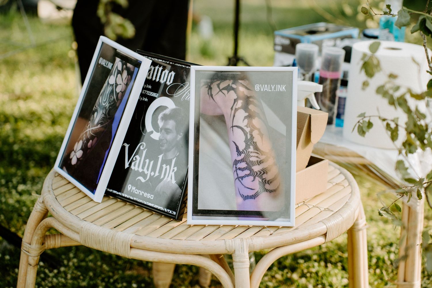 Valy Ink tattoo portfolio books displayed on a wicker table at an outdoor event.