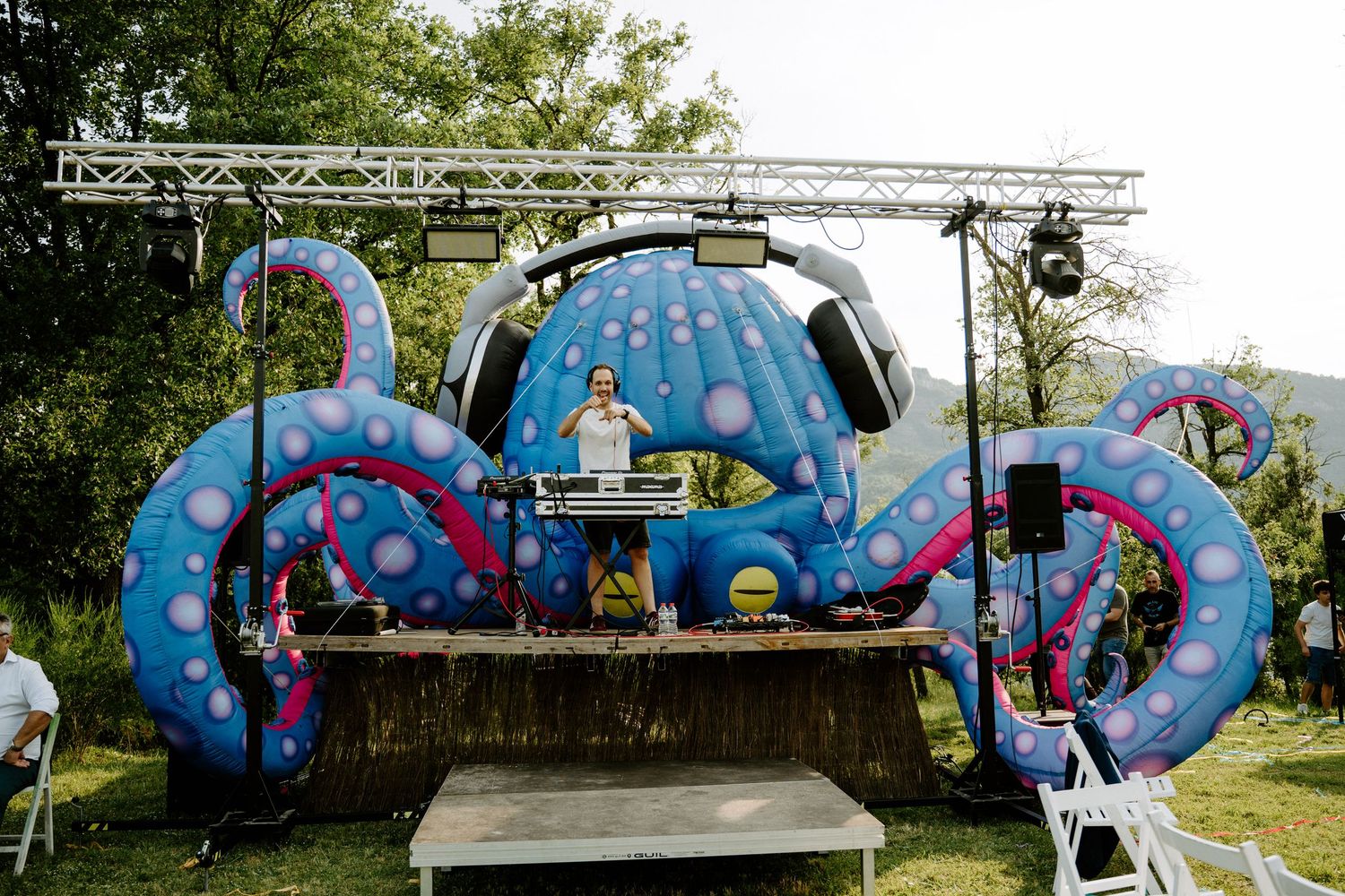 DJ performing on vibrant blue giant octopus themed stage setup at outdoor wedding reception.
