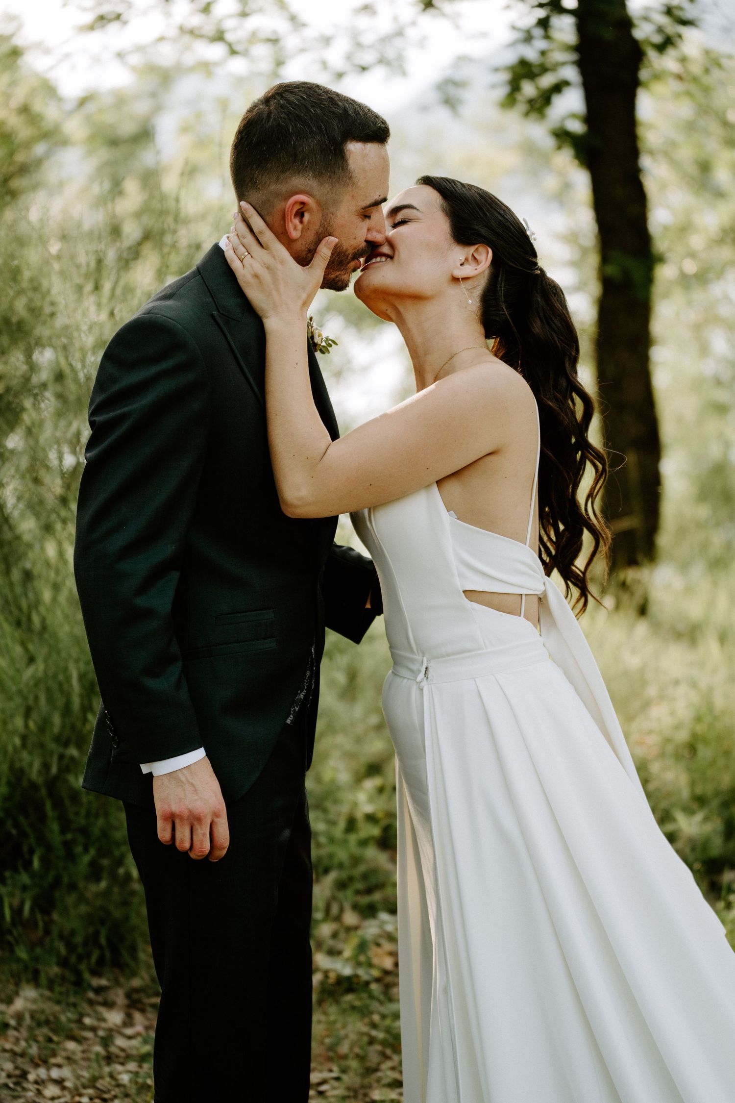Bride and groom sharing romantic almost-kiss moment surrounded by lush green forest.