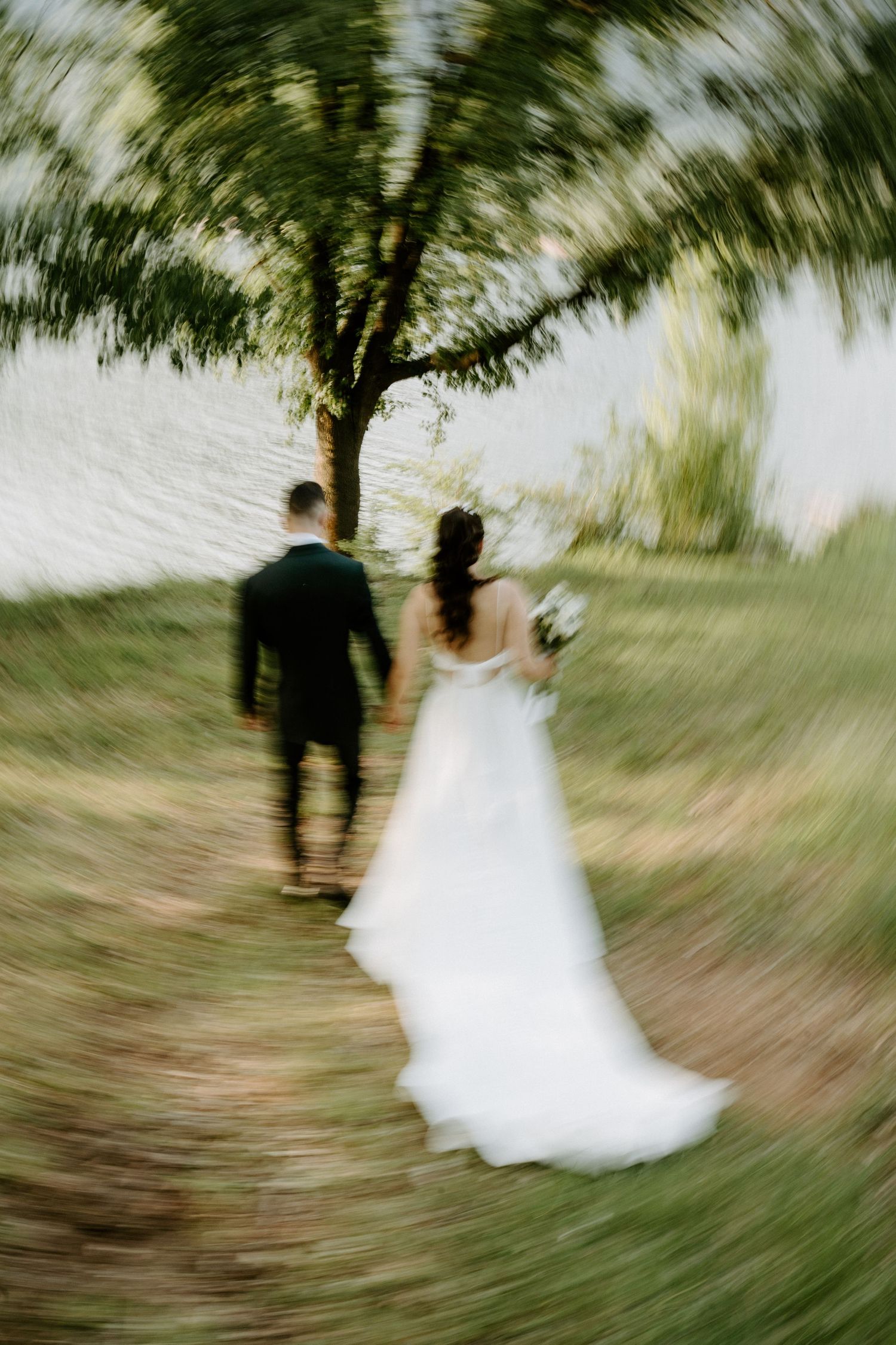A bride and groom walk hand in hand through a lush green path in a dreamy zoom-blur wedding photo.