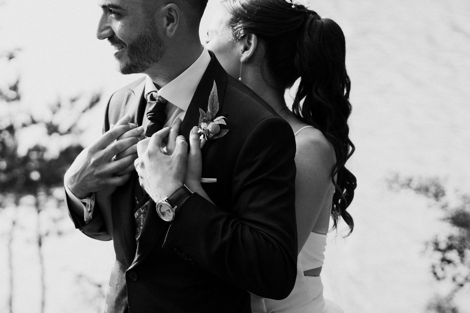 Black and white intimate portrait of bride embracing groom from behind outdoors.