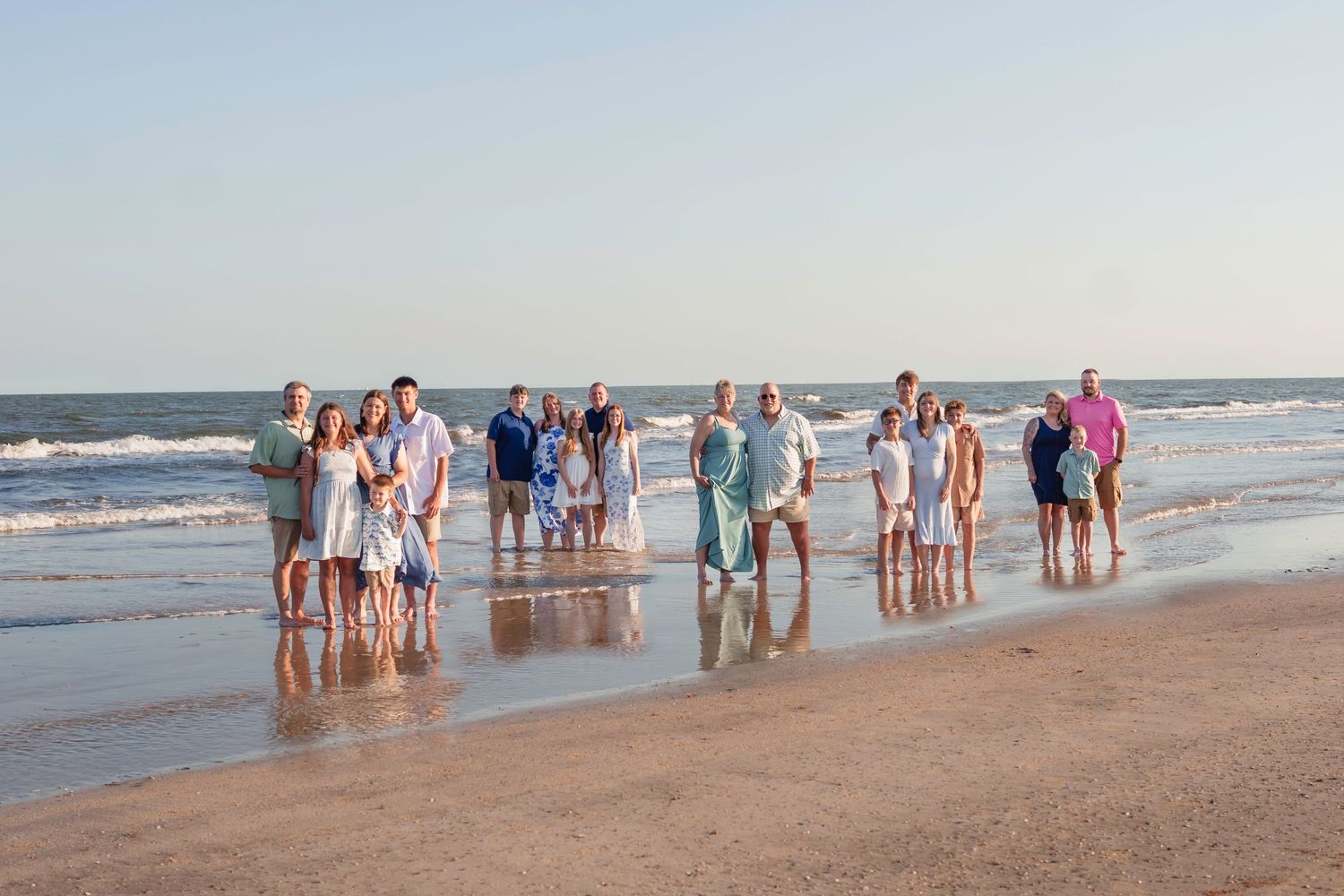 Large family group posing together on a sandy beach with ocean waves in the background during golden hour.