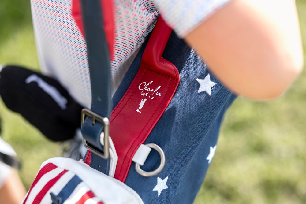 Close-up of a patriotic stars and stripes golf bag with a red Charlie logo detail and silver buckle strap.