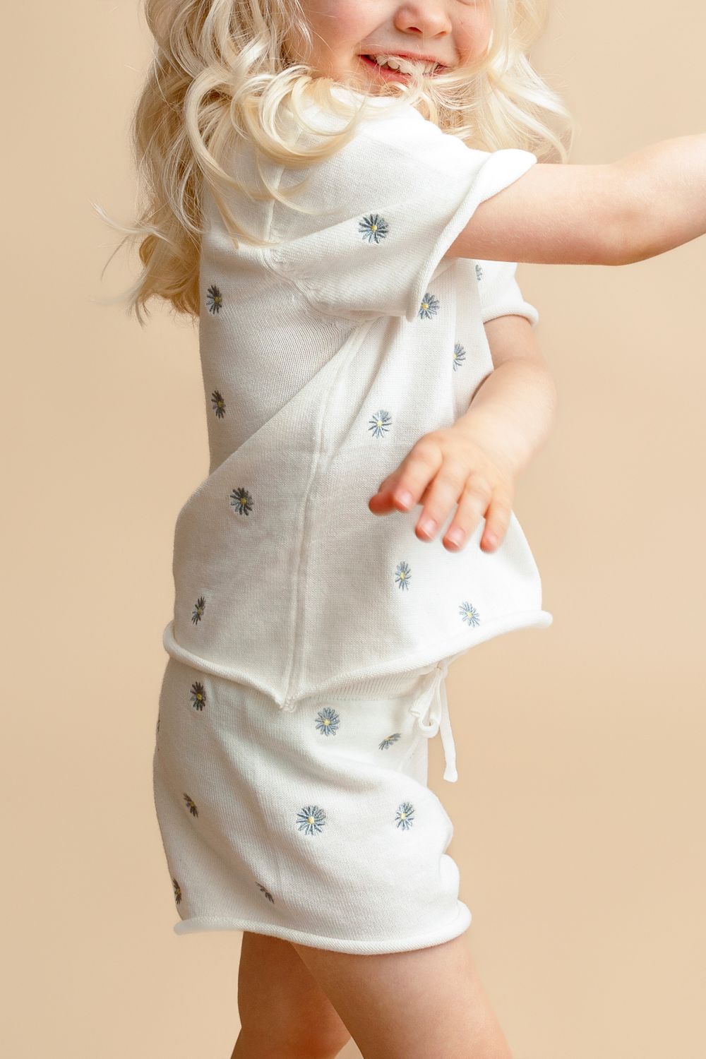 Toddler girl dancing in white floral print matching skirt set with short sleeves on beige background.