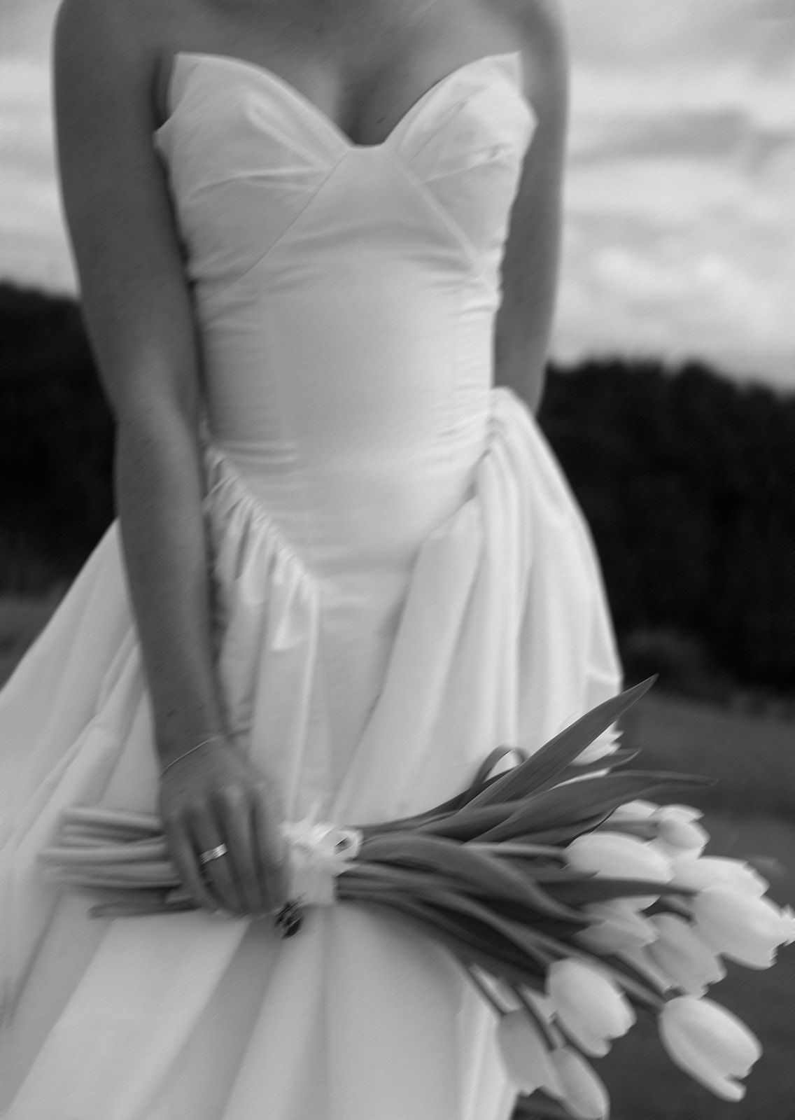 Bride in strapless white wedding gown holding a bouquet of white tulips, black and white photo.