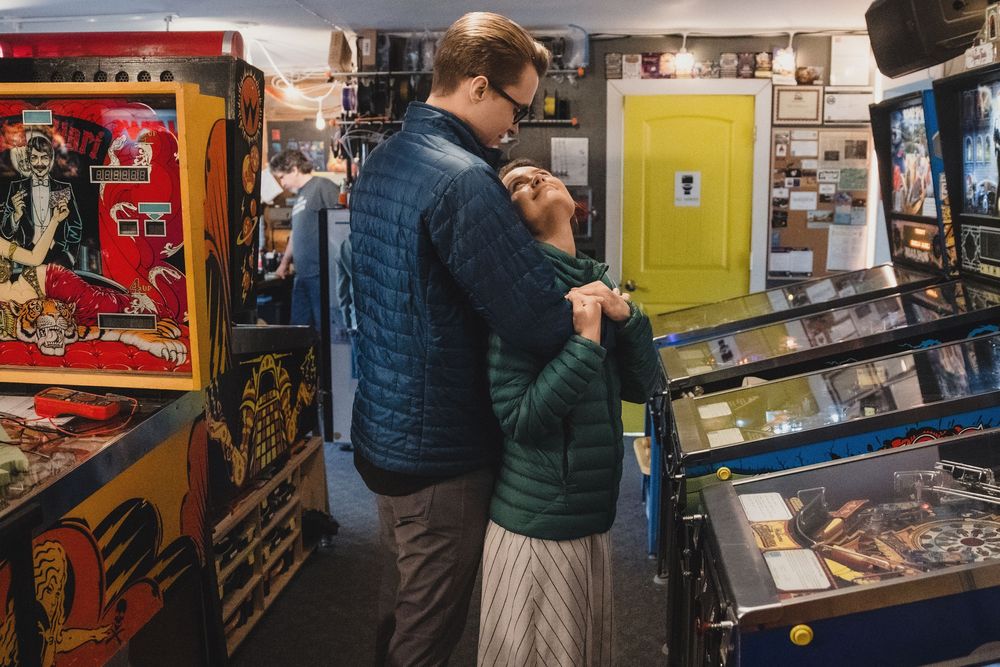 Couple embracing romantically among vintage pinball machines in a retro arcade game room.