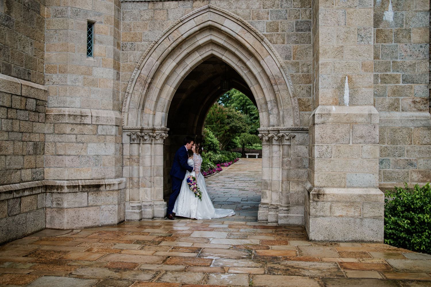 Bride and groom sharing a romantic moment under a Gothic stone archway at an elegant wedding venue.