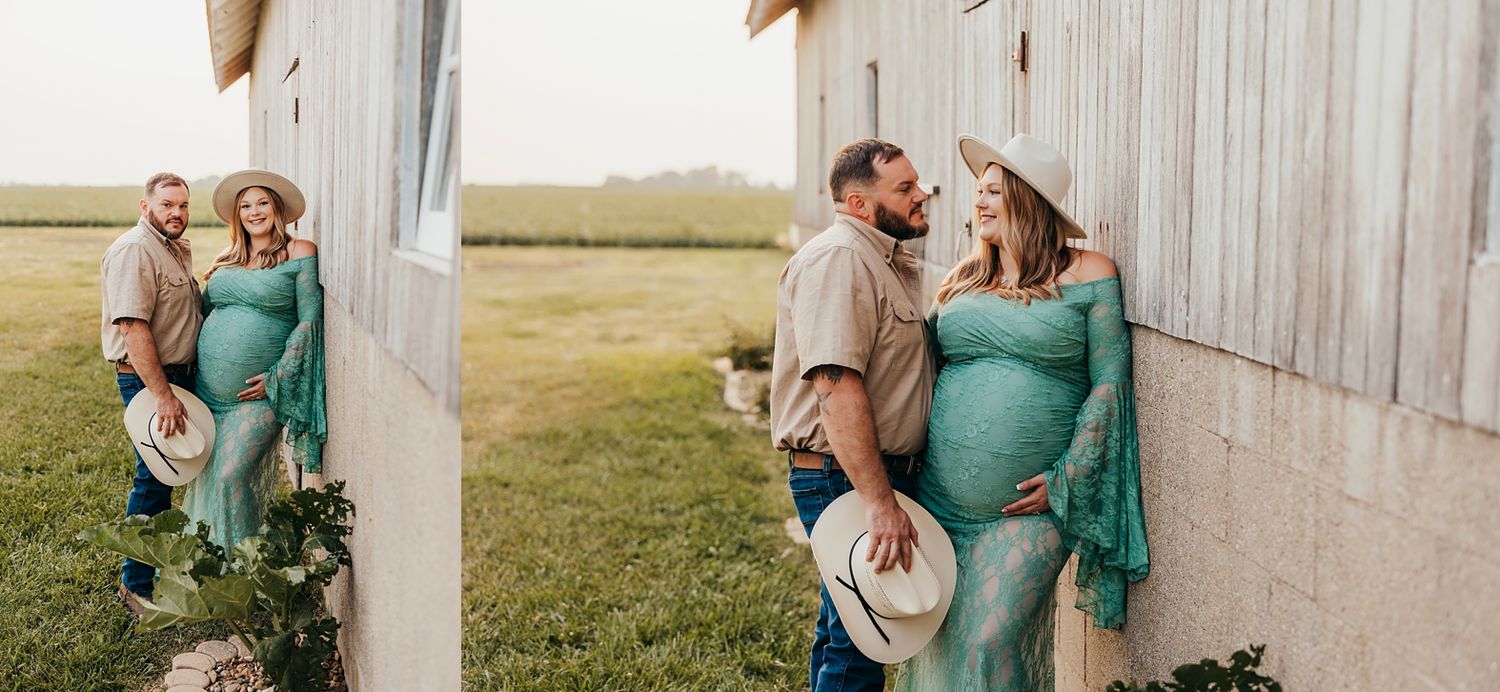 Couple posing for maternity photos outdoors near a barn, woman in teal lace dress with baby bump, man in casual country attire.