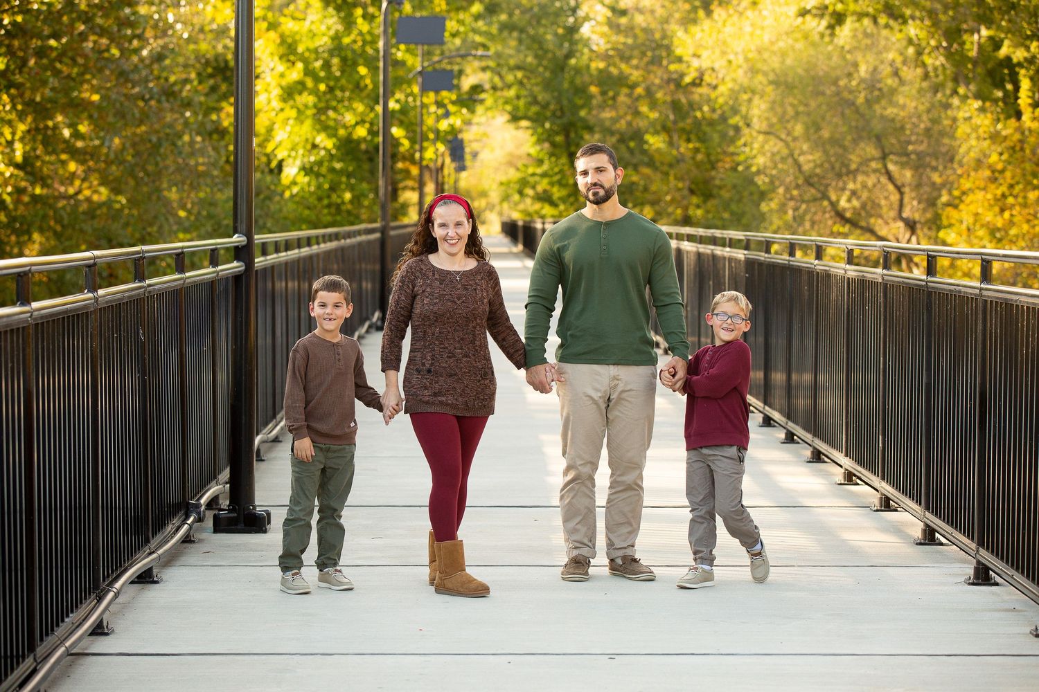Family of four posing by a peaceful river surrounded by autumn foliage during an outdoor fall photo session.