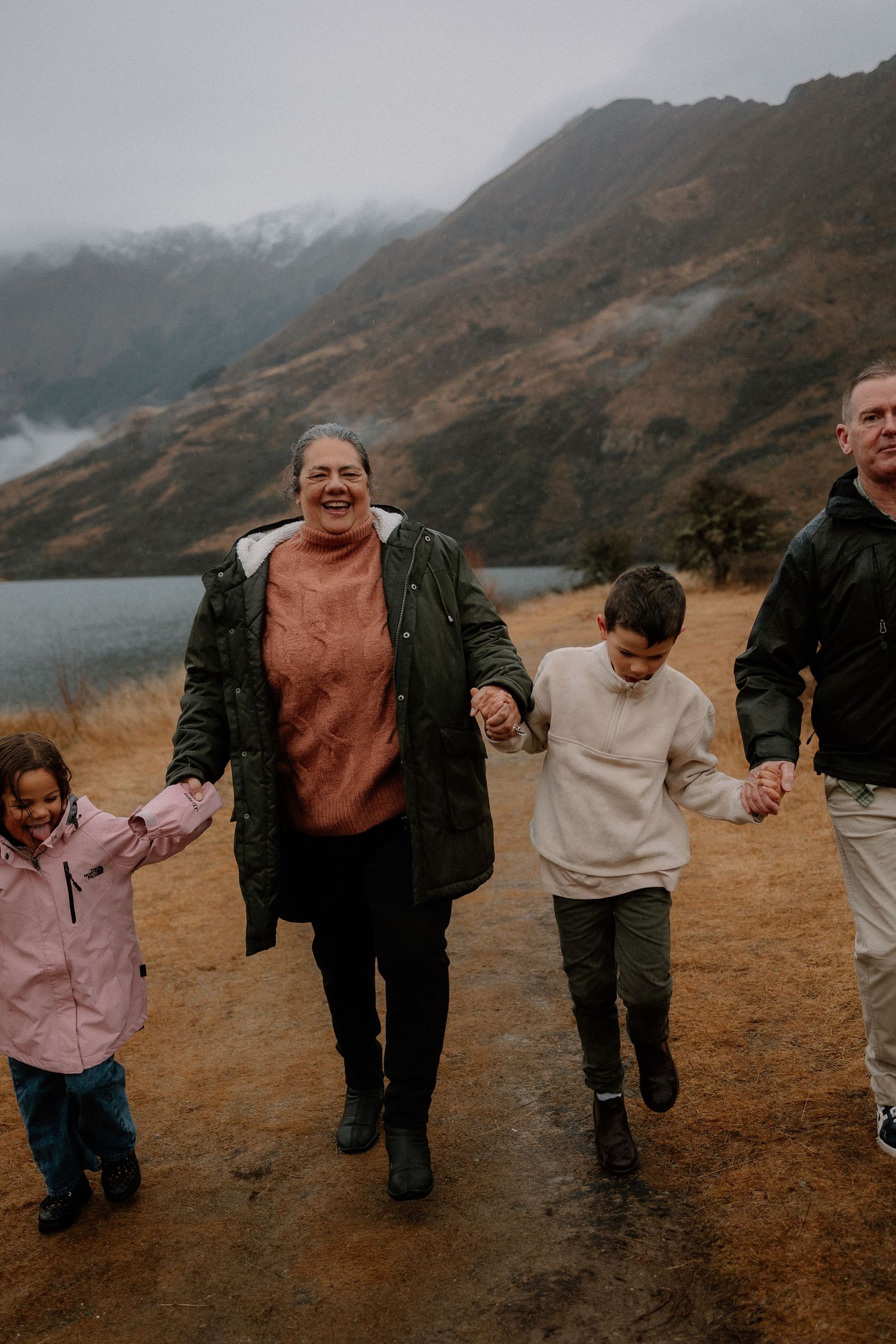 A smiling toddler girl held by a woman in a green sweater with misty mountains in the background.