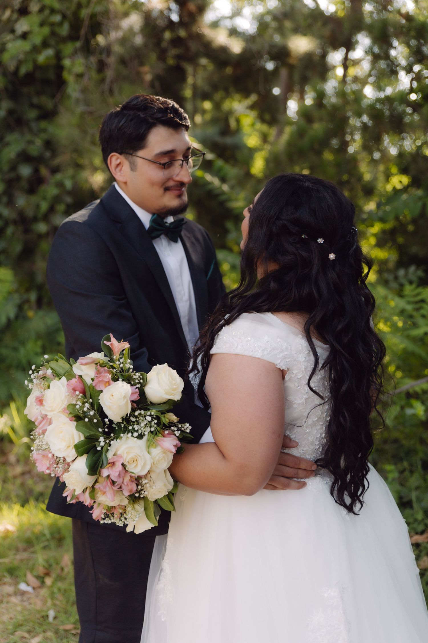 Wedding couple sharing a tender moment in a sunlit garden, bride holding a floral bouquet.