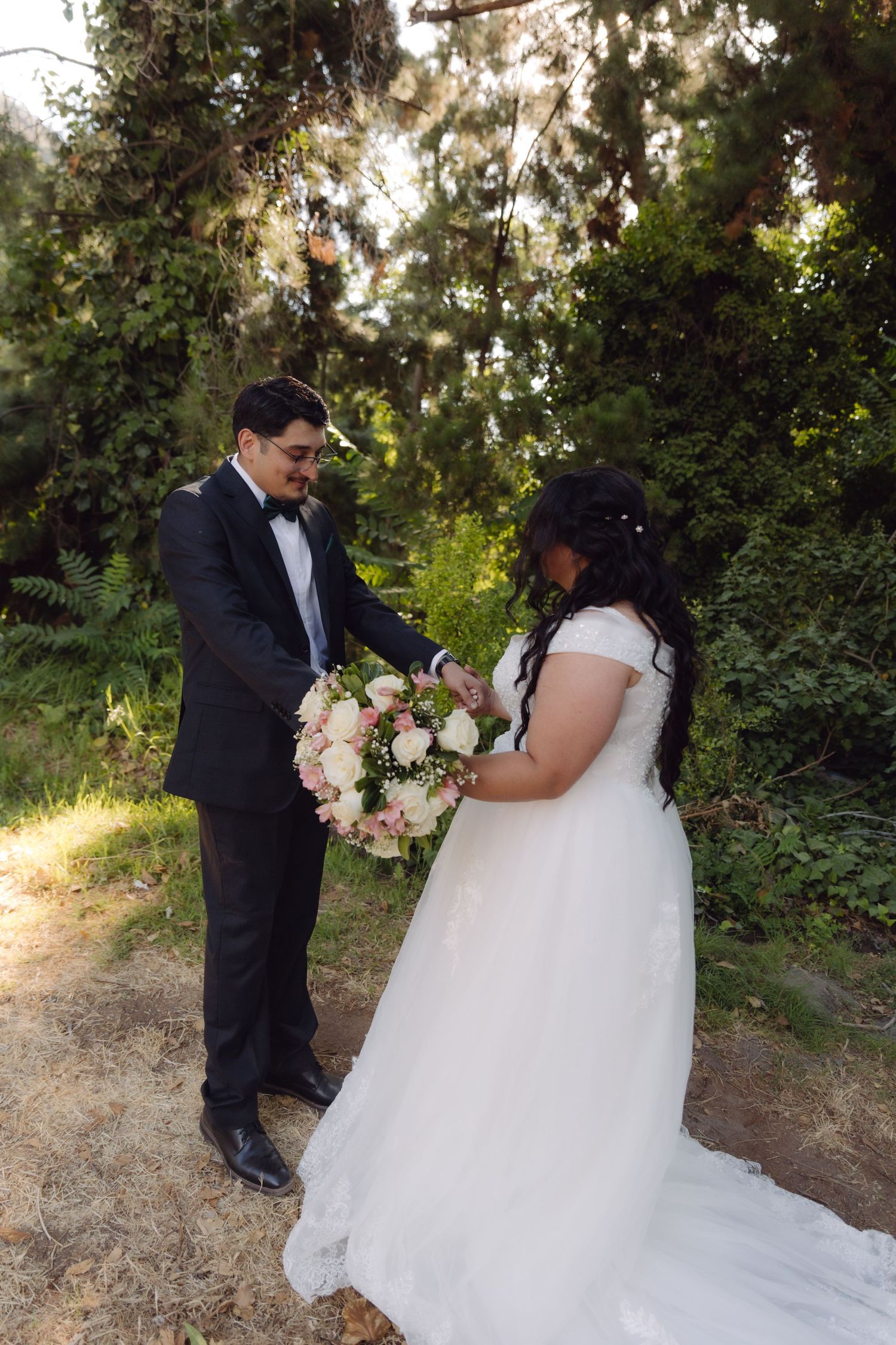 Groom presenting a pink and white floral bouquet to bride in a lush green garden setting.