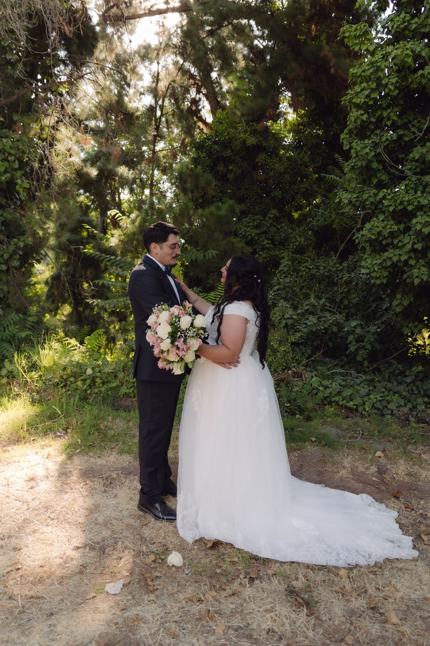 Wedding couple sharing a romantic moment in a sunlit garden, bride holding a pink bouquet.