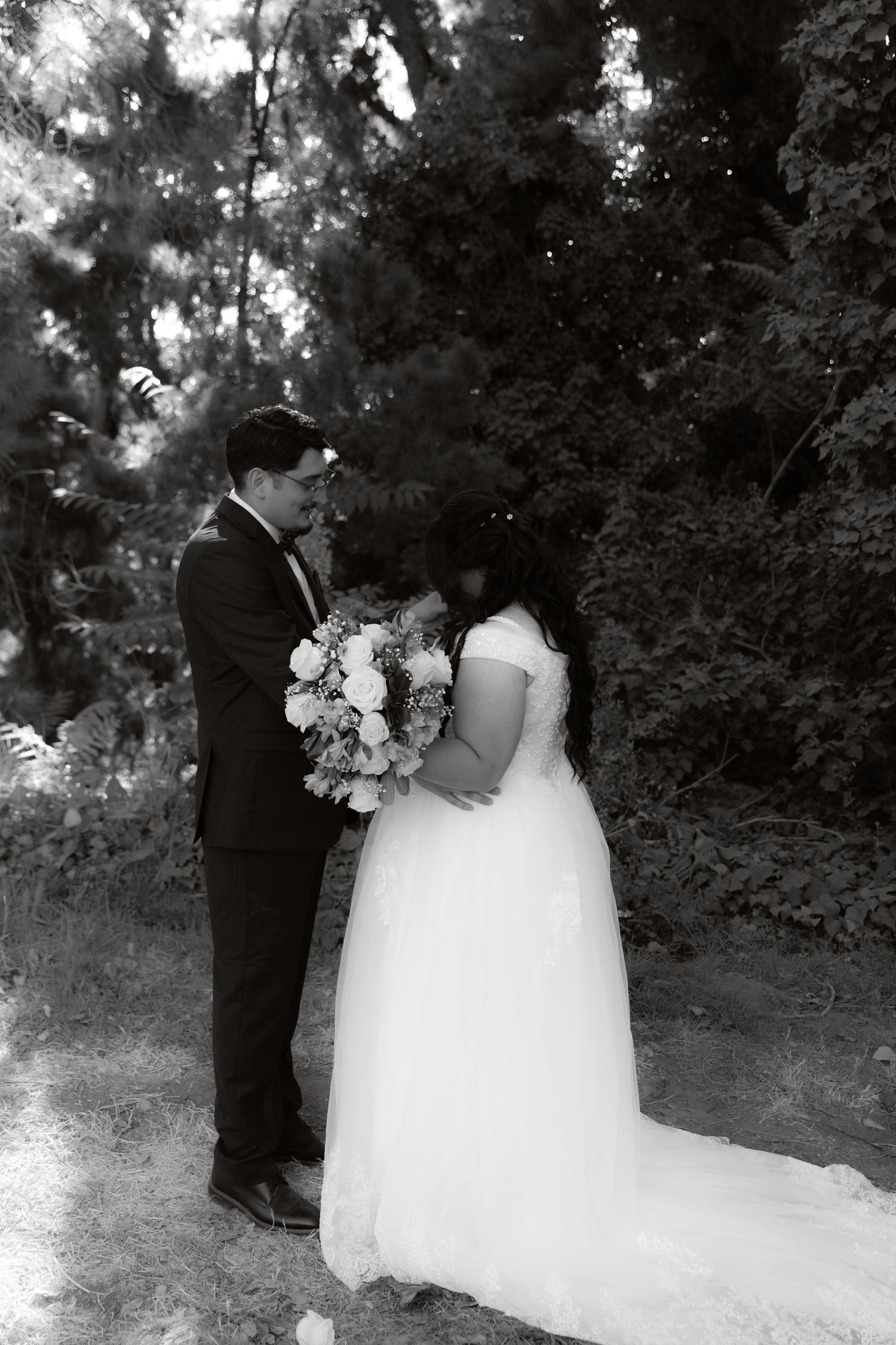 Black and white wedding portrait of couple embracing in a lush forest with floral bouquet.