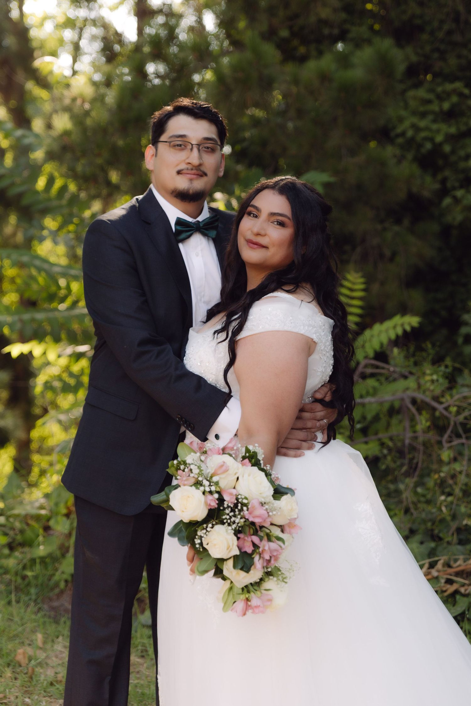 Wedding couple posing together in garden, bride holding pink and white floral bouquet.