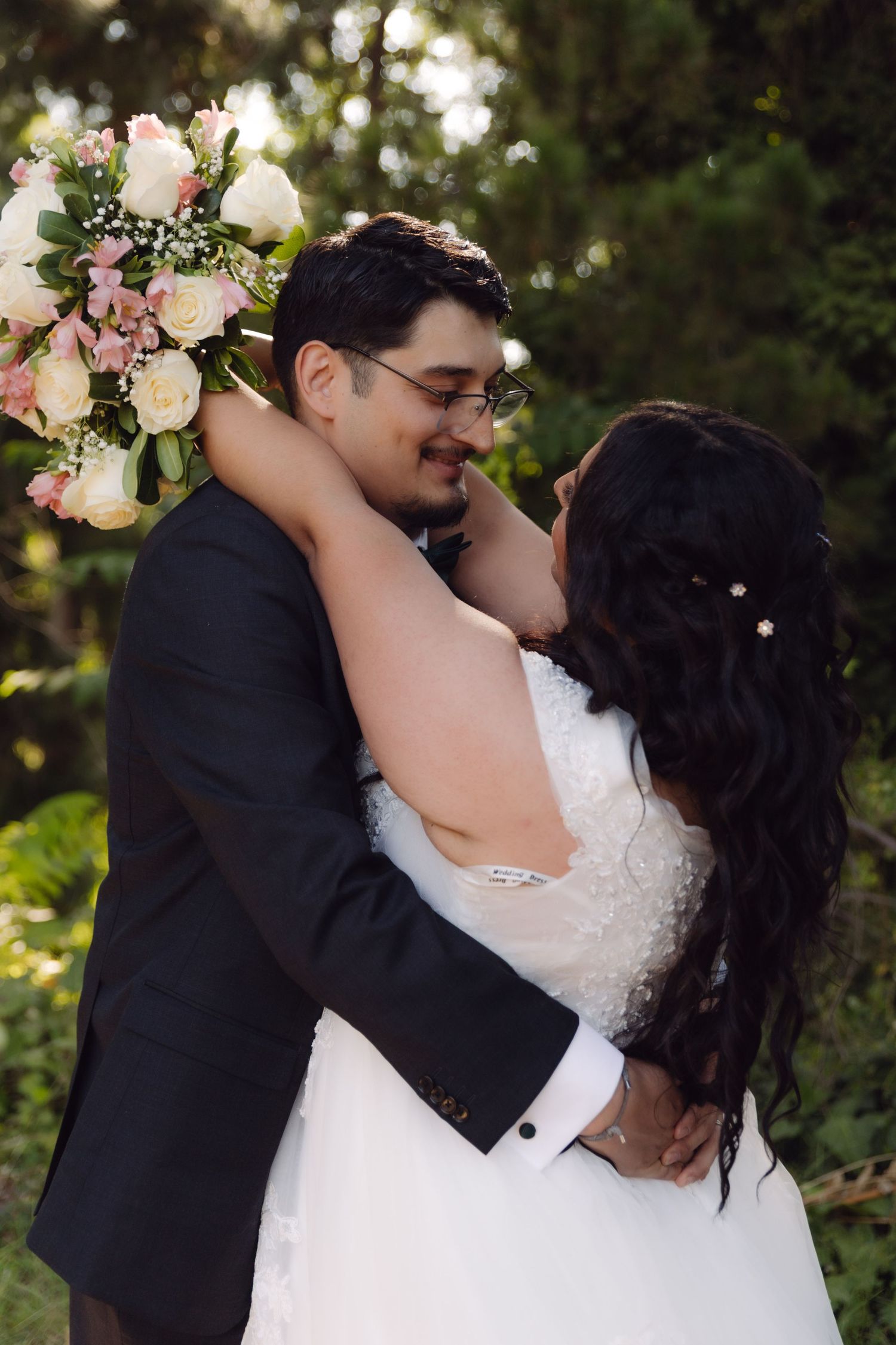 Smiling groom embraced by bride in lush garden, bride holding colorful floral bouquet.