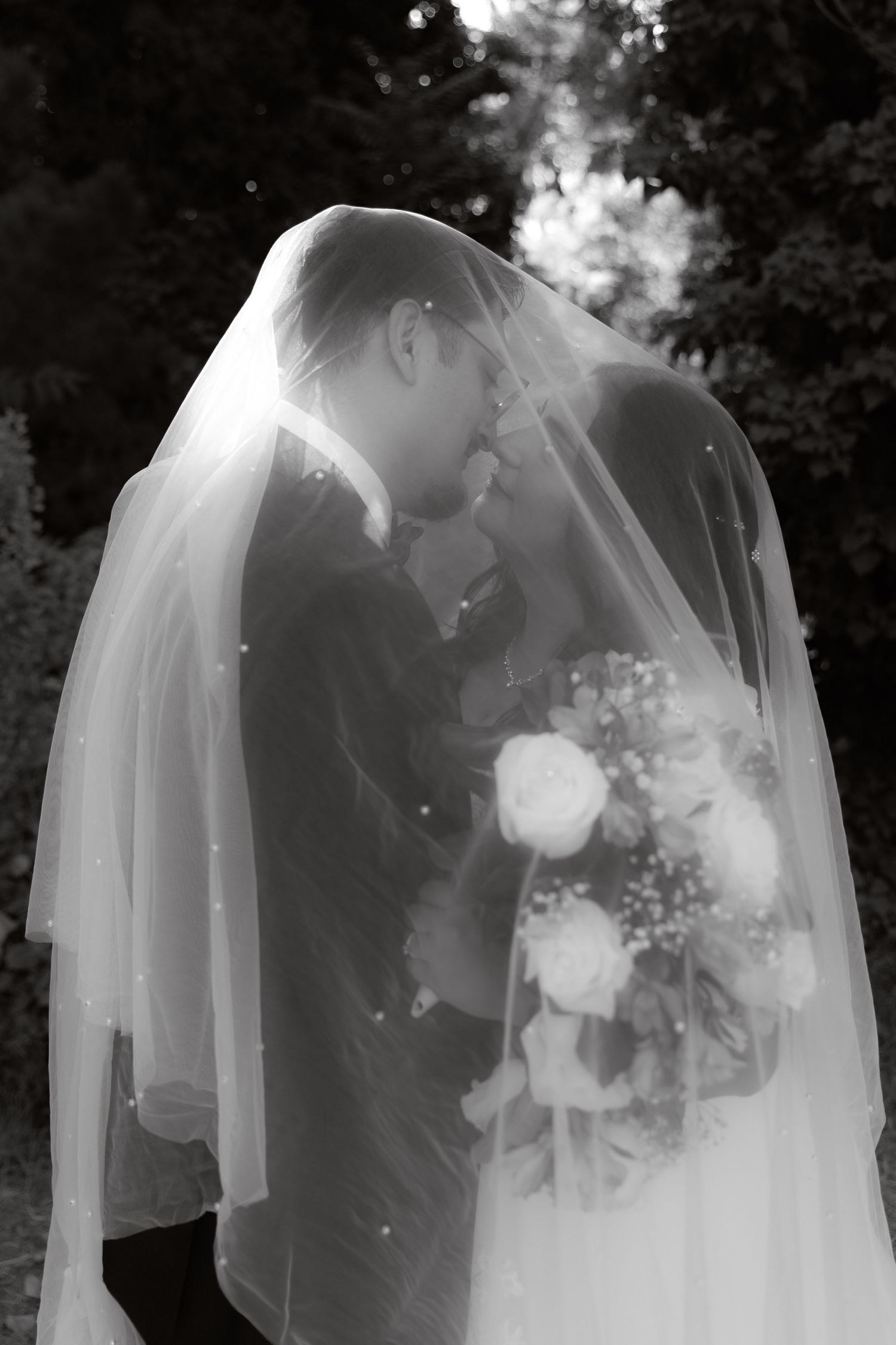 Black and white romantic wedding portrait of couple kissing under flowing bridal veil.