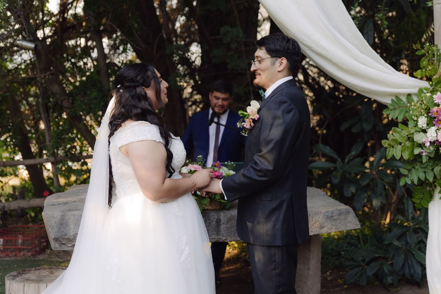 Bride and groom holding hands during outdoor garden wedding ceremony under decorated arch.