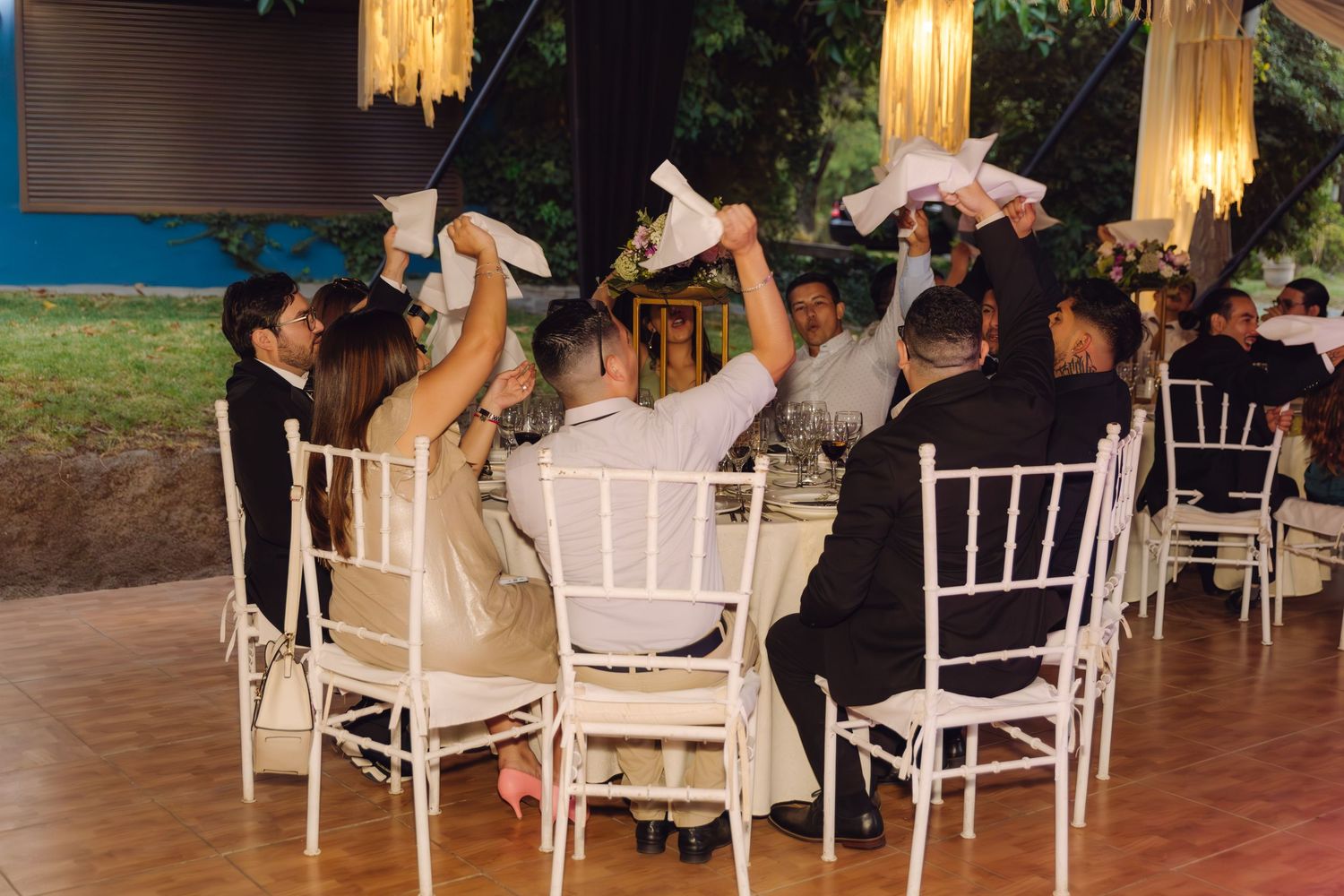 Wedding guests wave white napkins in celebration at elegantly decorated indoor reception venue at night.