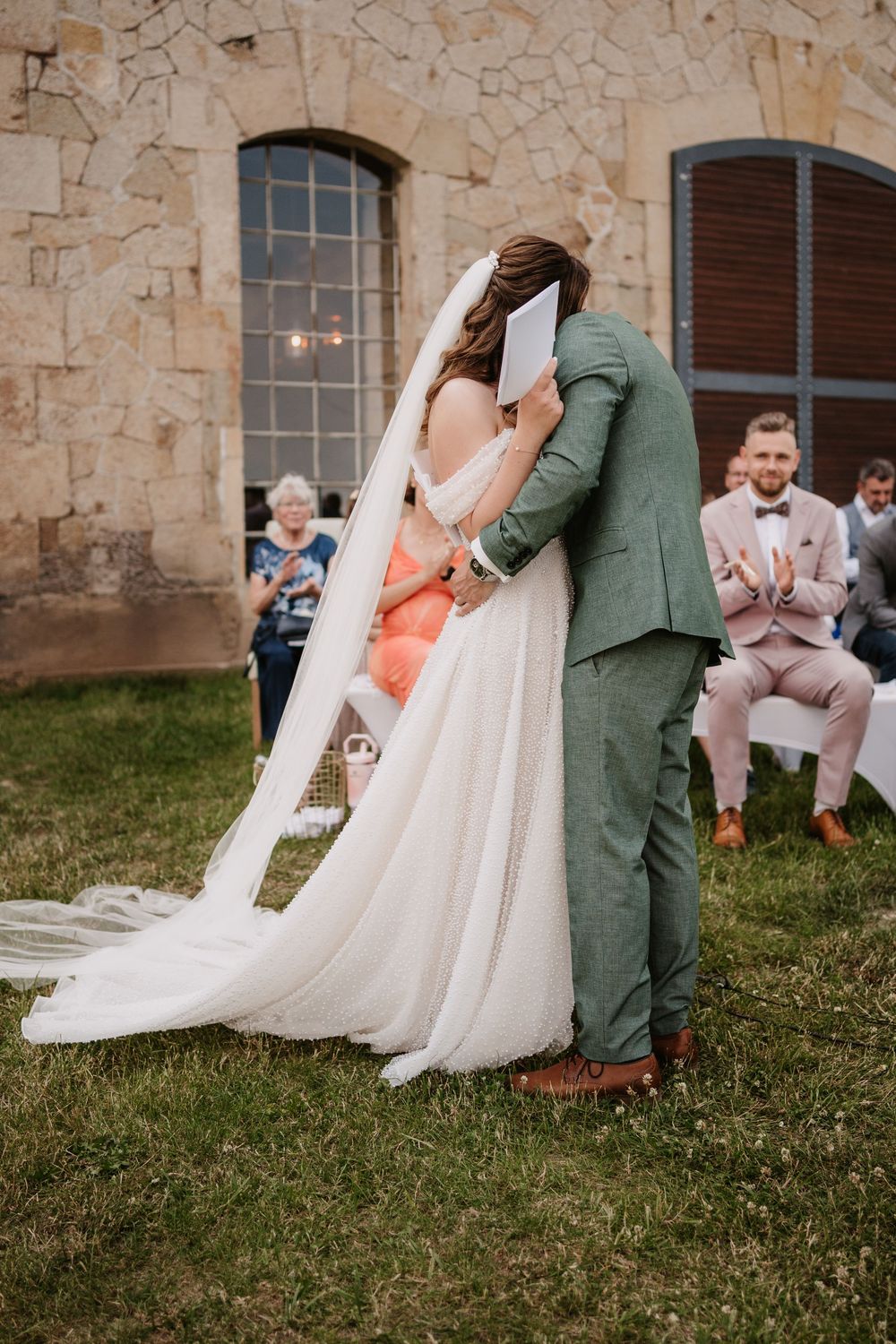Bride and groom sharing a kiss during outdoor wedding ceremony with guests seated behind.