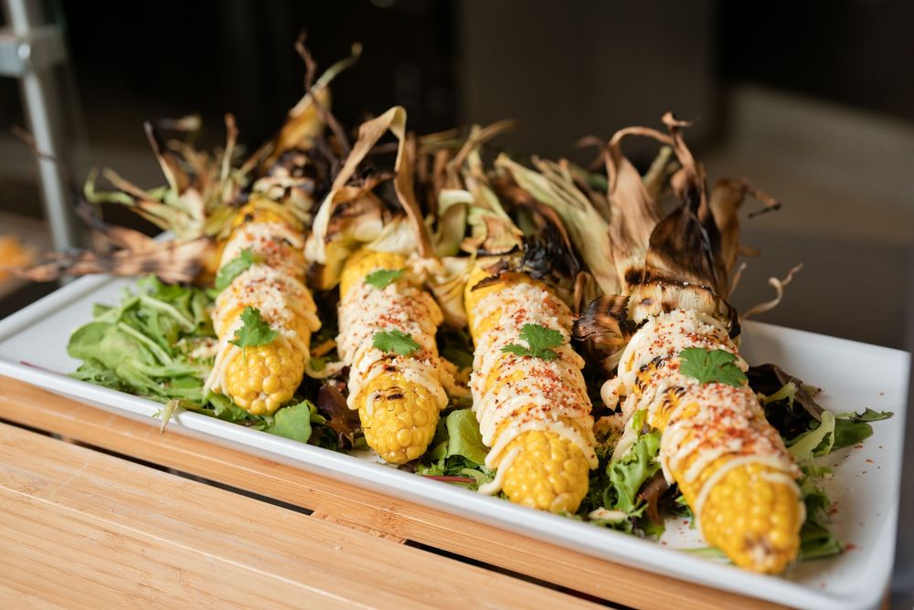 Grilled corn on the cob with toppings served on a white platter with greens.