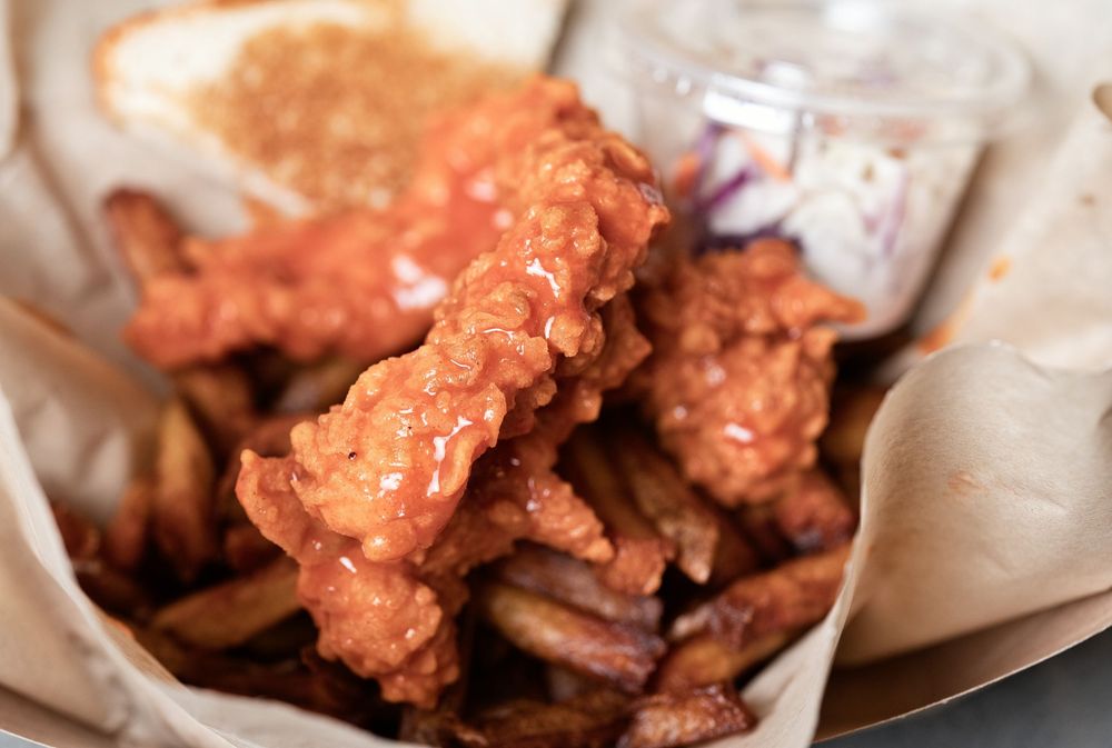 Crispy Nashville hot chicken tenders served over seasoned fries in a paper-lined basket with a side of coleslaw.