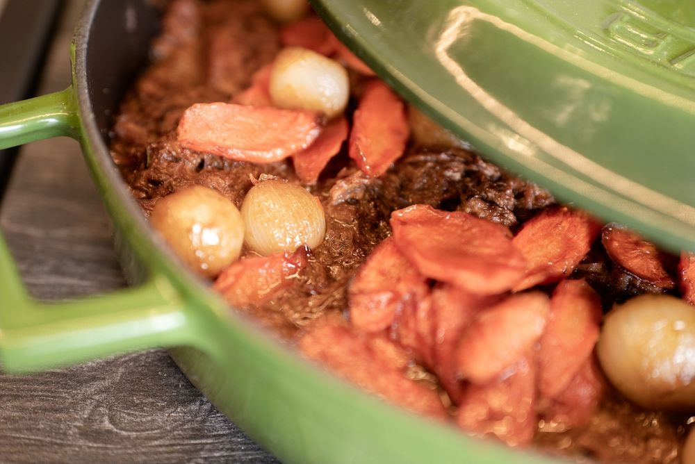 Green Dutch oven filled with beef stew, carrots, and pearl onions slow-cooked to perfection.