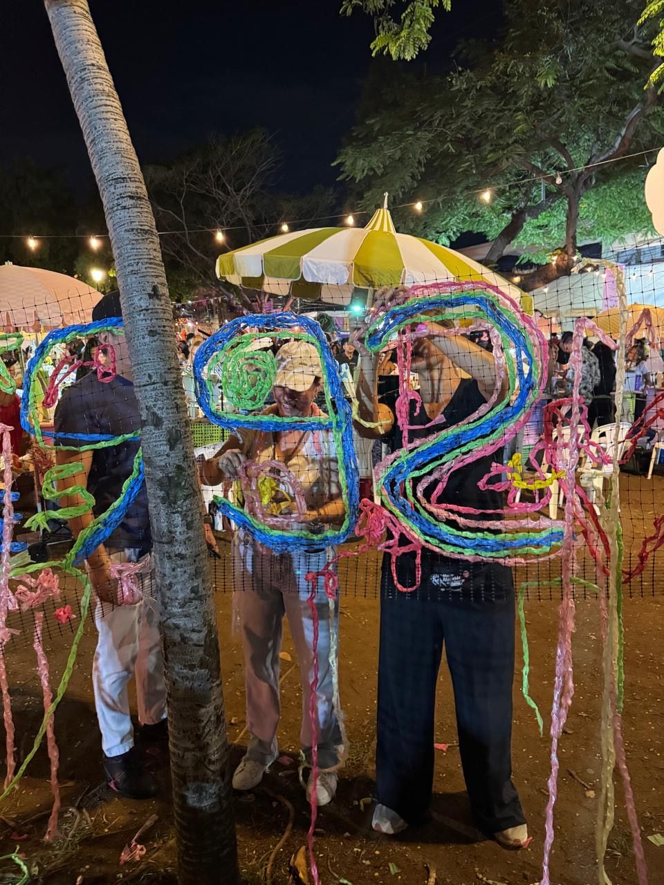 Colorful pinata numbers at a festive night market with string lights and yellow umbrella in background.