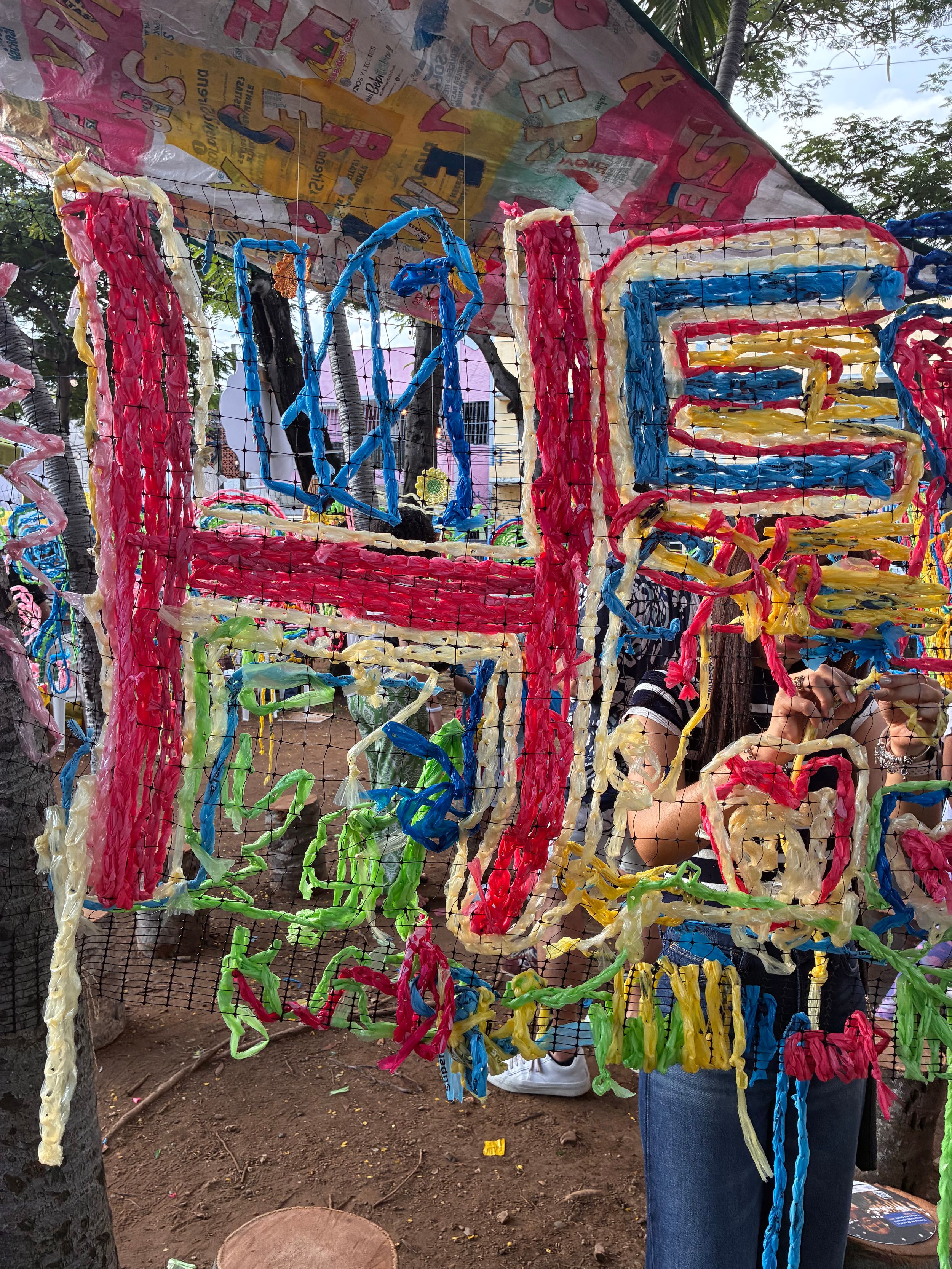 Colorful yarn art installation with letters H and E woven in red and blue at an outdoor festival.