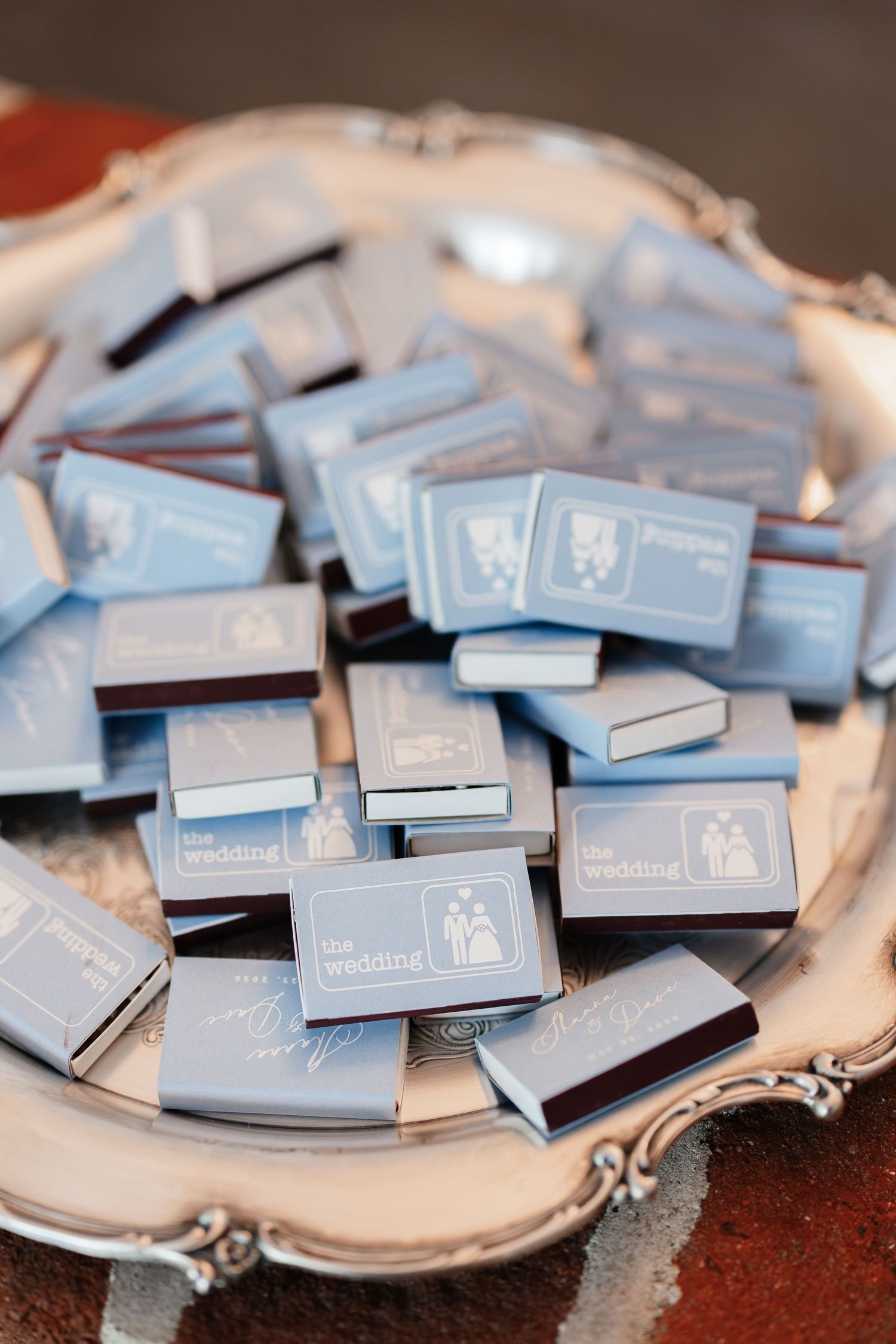 Blue wedding matchbox favors with couple illustration piled on silver tray for guests.