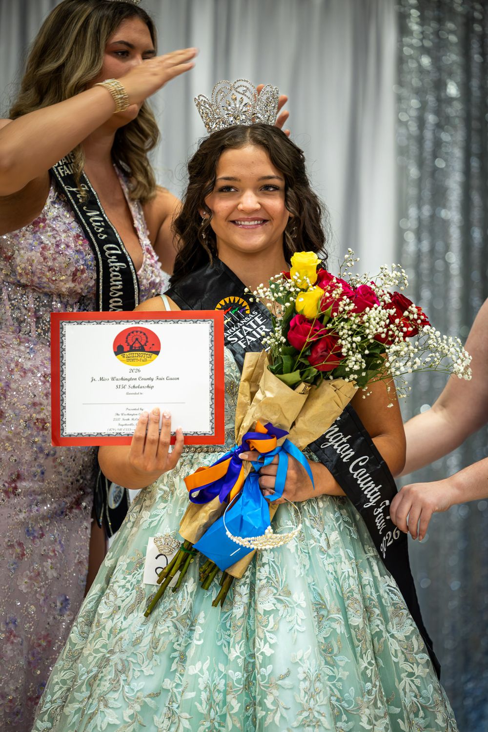 Young girl in mint green gown smiles holding roses and certificate after winning Jr. Miss Washington County Fair Queen pageant.
