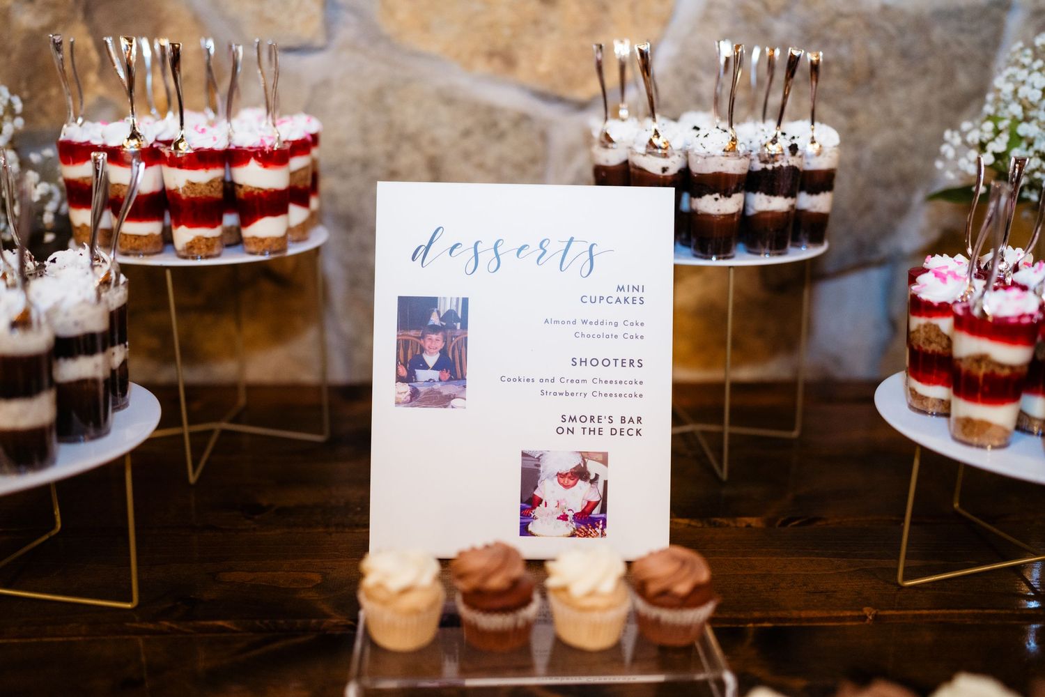 Elegant wedding dessert table featuring layered parfaits, cupcakes, and a decorative menu sign at a rustic venue.