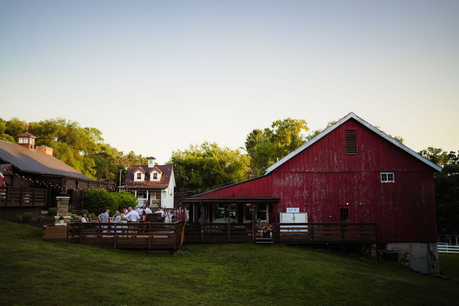 Rustic red barn and white farmhouse venue with green lawn at golden hour.