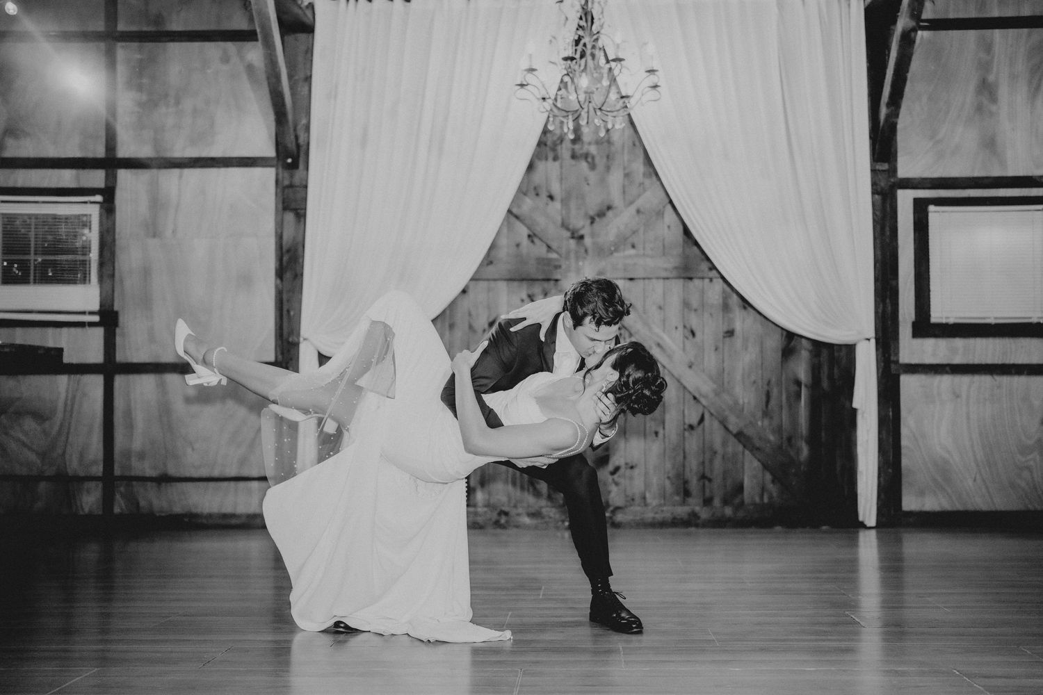 Black and white photo of bride and groom sharing a romantic dip dance at rustic barn wedding reception.