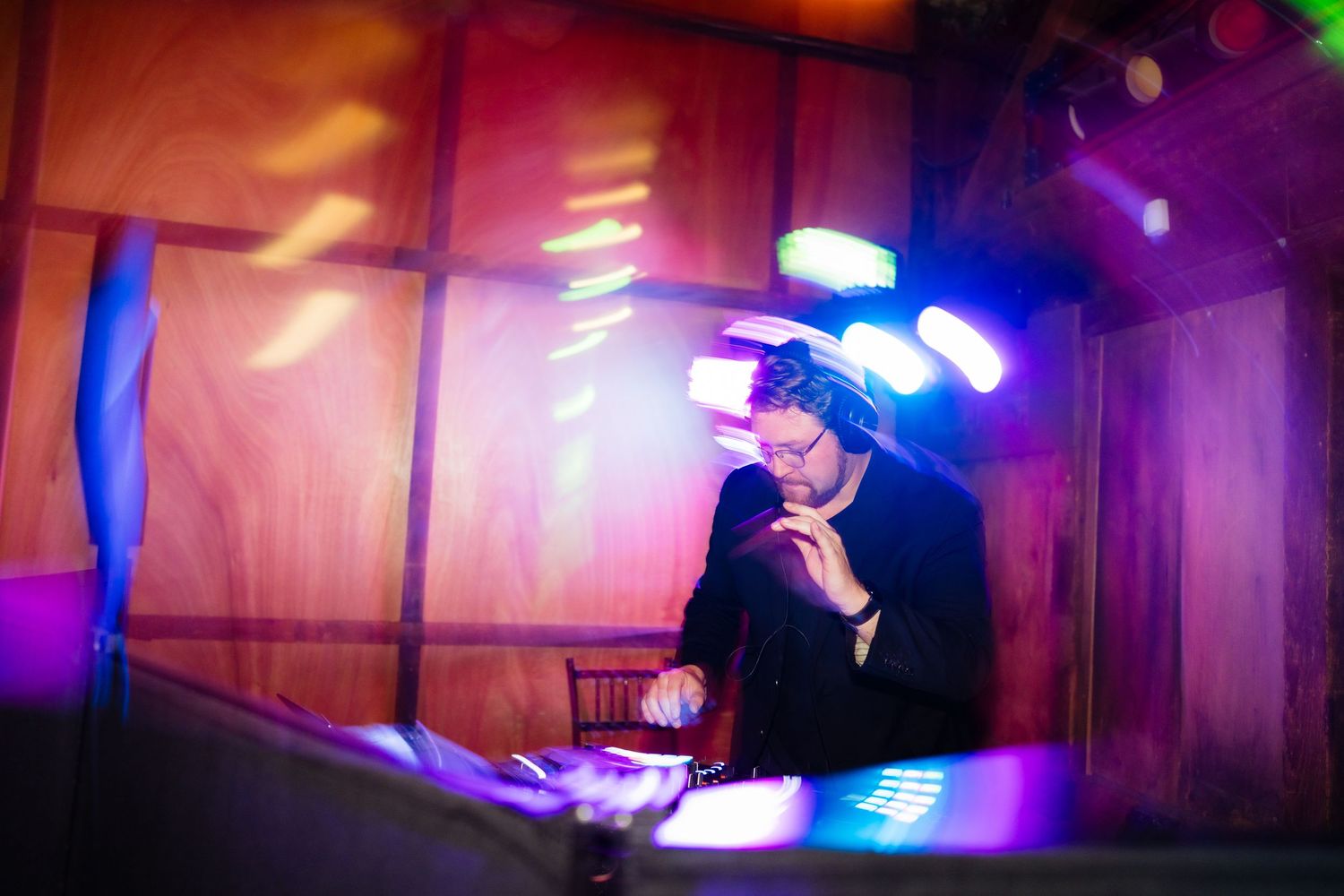 DJ performing at a vibrant nightclub event under colorful stage lights in a wood-paneled venue.