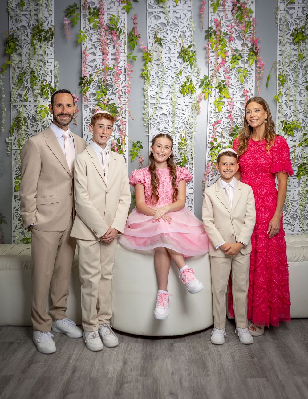 Family of five posing elegantly in formal attire with floral backdrop, featuring pink and beige outfits.
