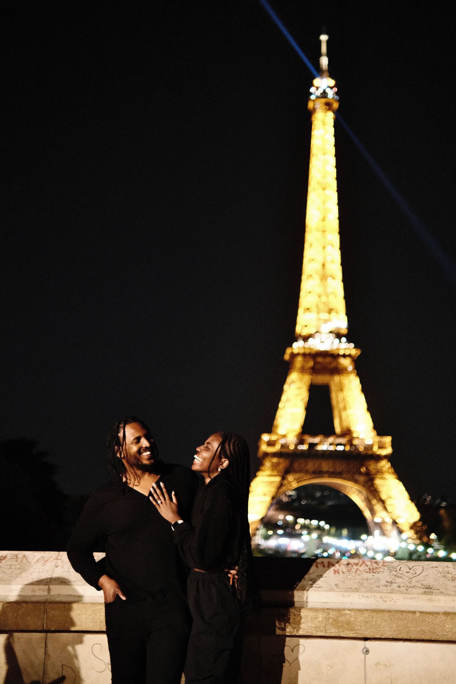 Couple embracing at night in front of the illuminated Eiffel Tower in Paris, France.