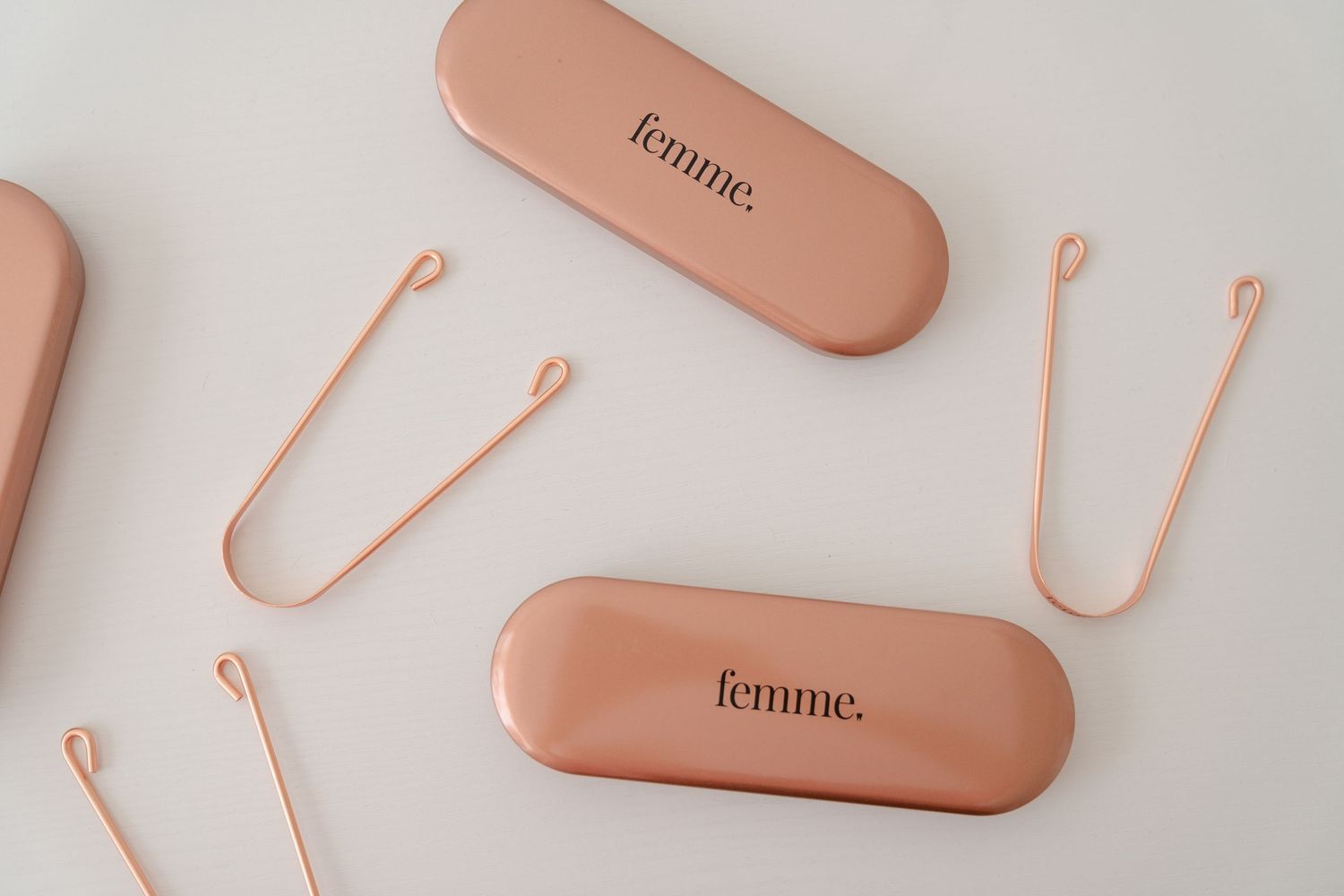 Pink 'femme.' branded tongue scrapers with rose gold cases arranged on a white background.