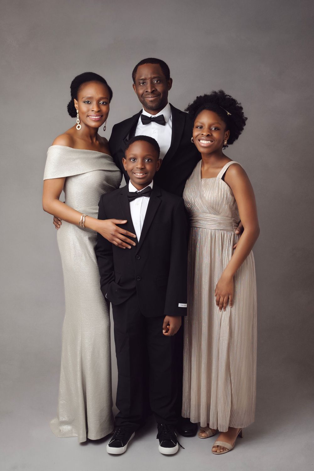 Elegant family of four posing in formal attire, wearing silver gowns and tuxedos, for a studio portrait.