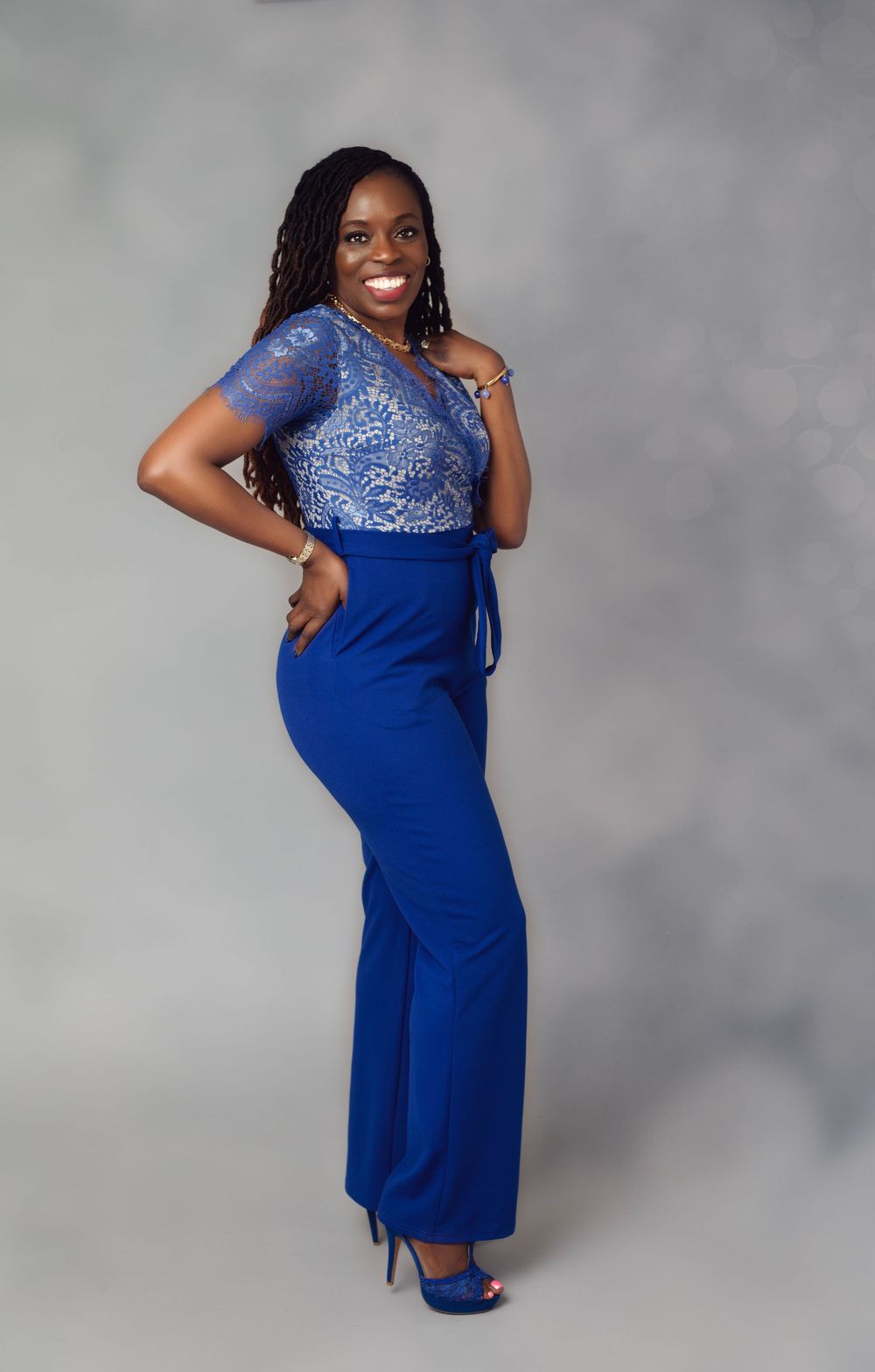 Woman in royal blue lace jumpsuit and heels posing confidently for a professional portrait photo.