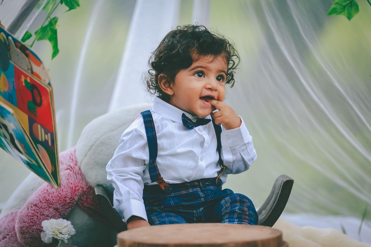 Young child sitting on grass beside a large teddy bear and wicker basket in front of a decorated teepee tent outdoors.