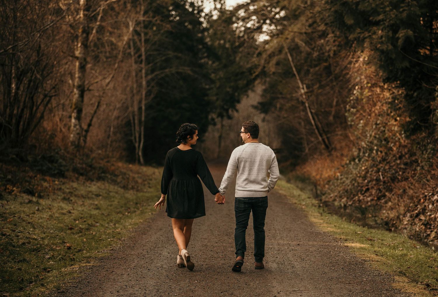 Couple holding hands walking down a scenic forest path surrounded by autumn trees near Mt. Rainier.