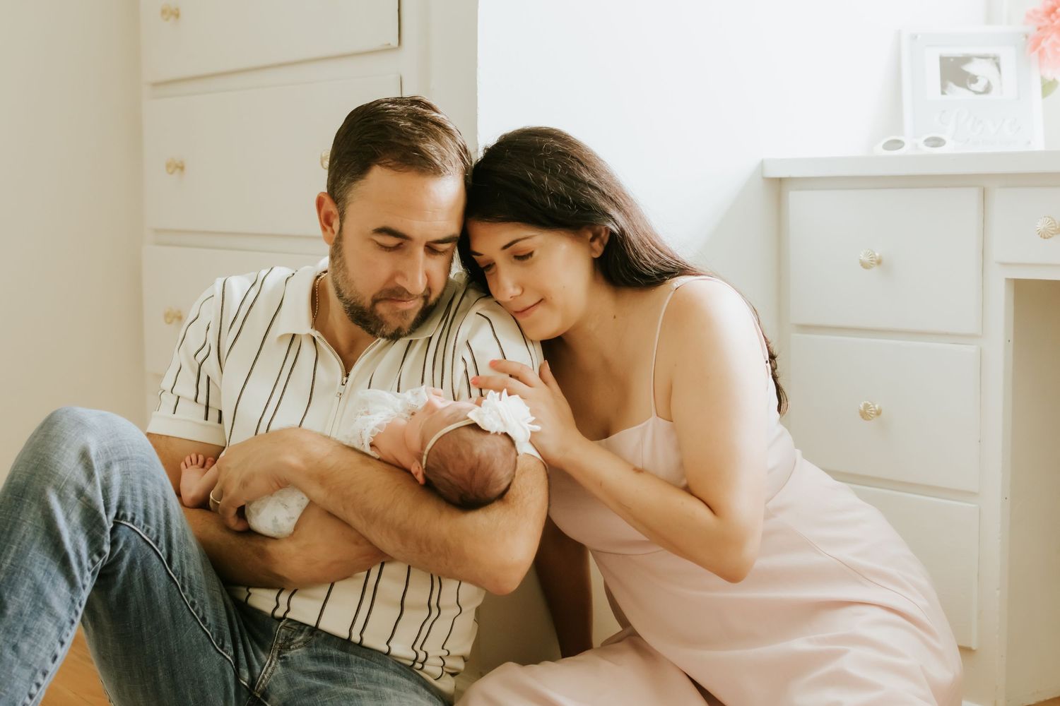 A couple sits together admiring their newborn baby, with the father cradling the infant in a cozy nursery room. newborn photos in home