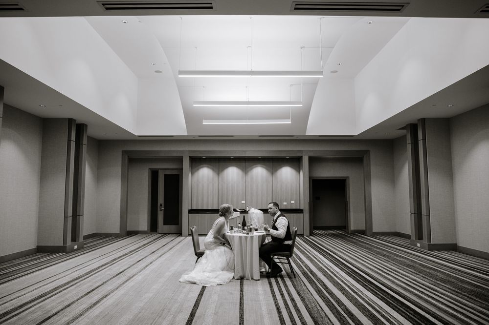Black and white photo of bride and groom sharing a private moment at a table in an elegant ballroom.