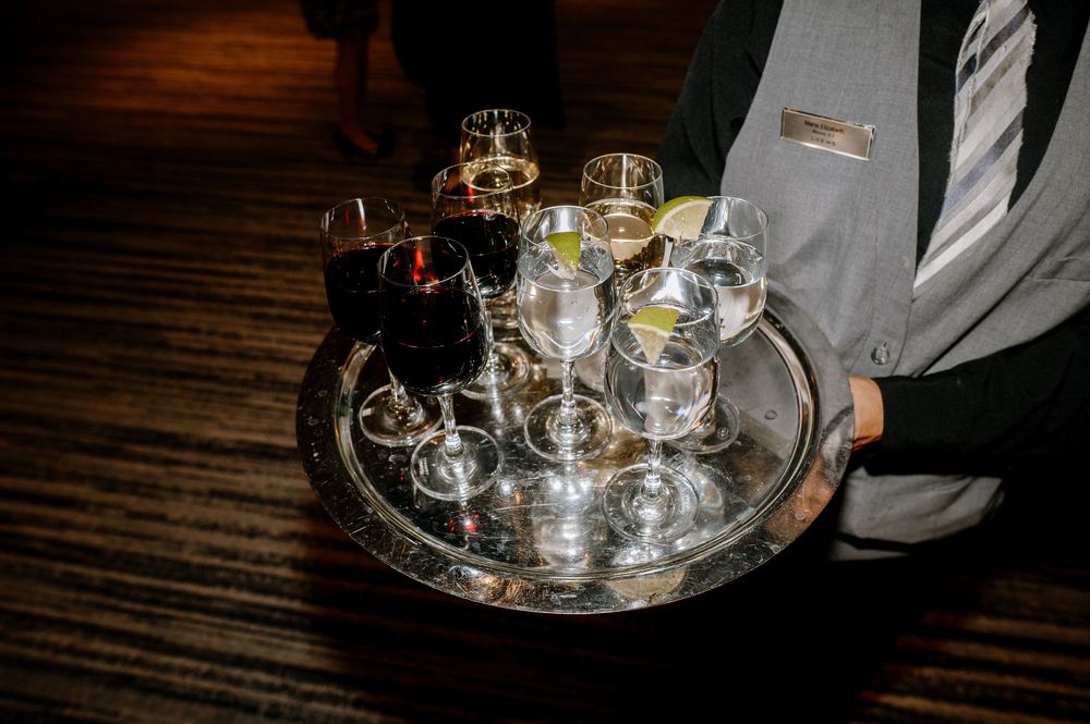 Waiter carrying silver tray with assorted wine and cocktail glasses at elegant wedding reception.