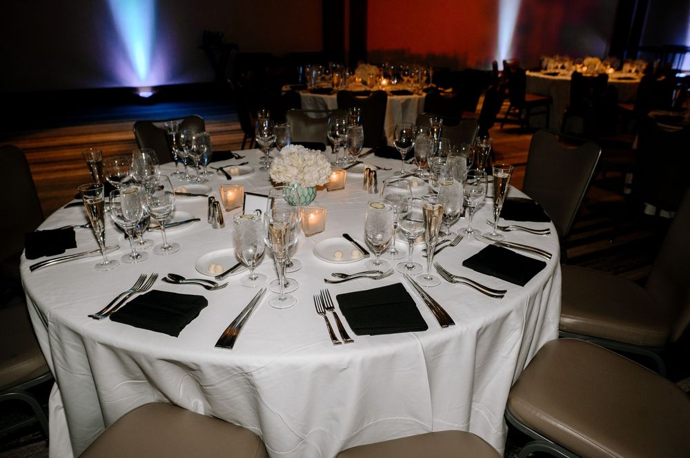 Elegant round banquet table set with white linens, black napkins, crystal glassware, and floral centerpiece for a formal event.