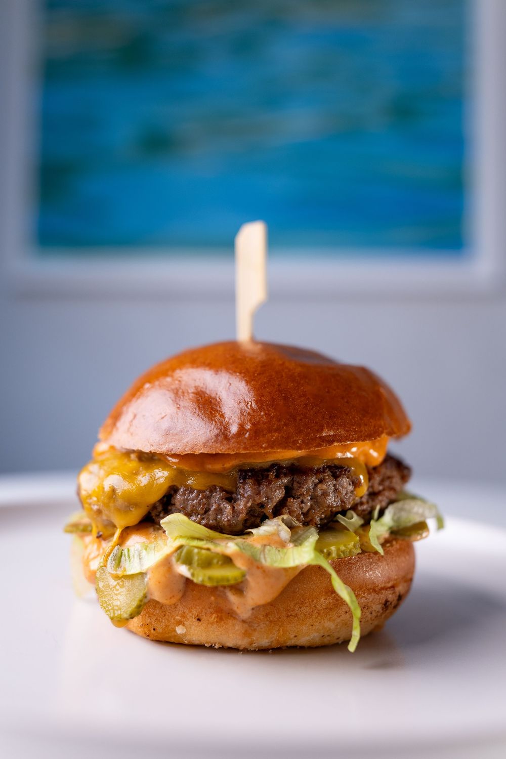A juicy cheeseburger with melted cheddar, lettuce, and special sauce on a toasted brioche bun, served on a white plate.