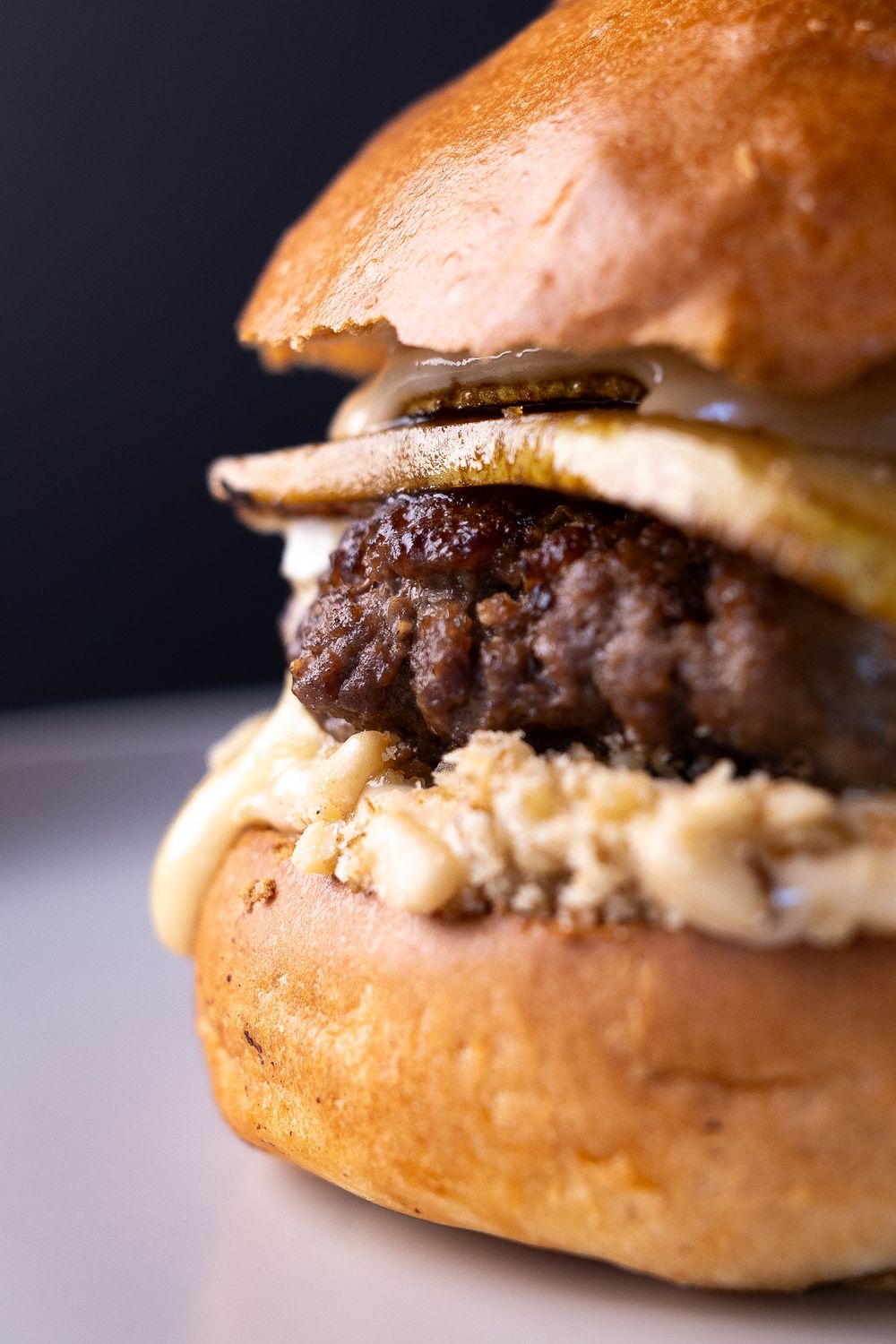 Close-up of a gourmet burger with a juicy beef patty, creamy sauce, and caramelized onions on a toasted brioche bun.