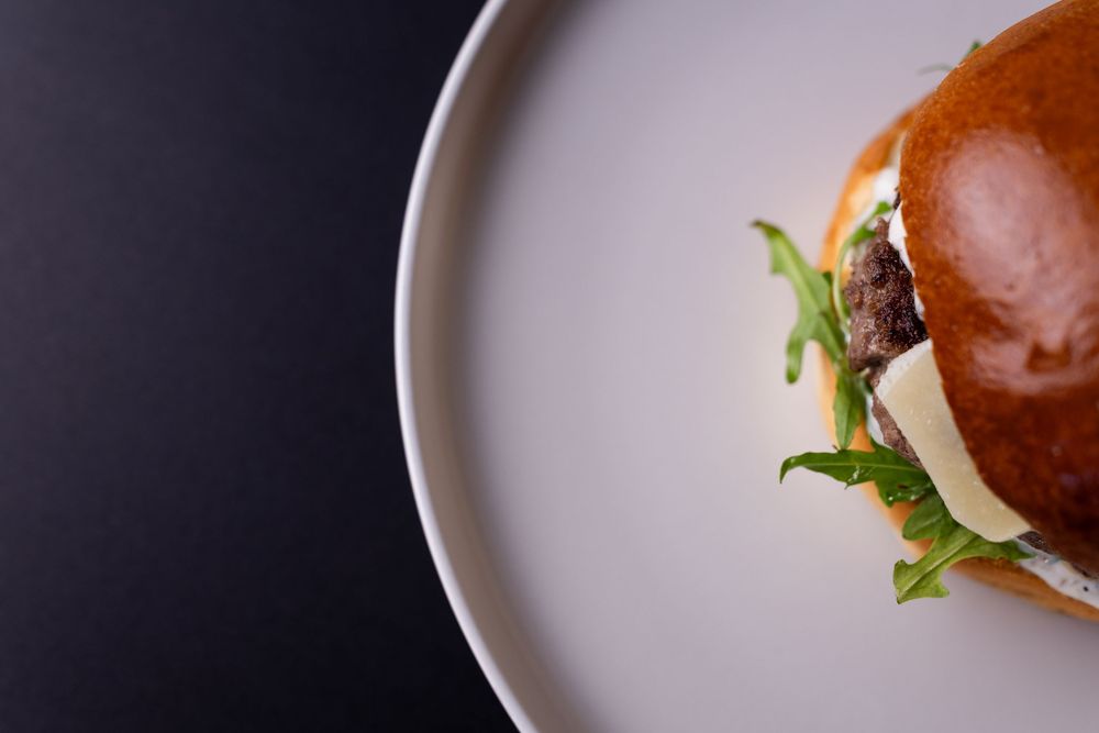 Gourmet burger with melted cheese and arugula on a brioche bun, served on a white plate.